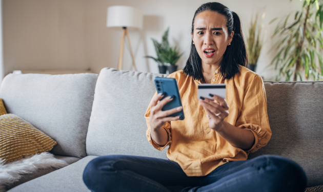 A pet sitter sits with an upset, shocked expression on her face looking at her credit card and cellphone.